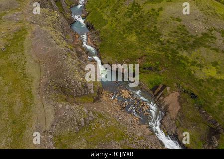 Gorge islandaise avec rivière qui coule rapidement vue d'en haut montrant des roches volcaniques escarpées et de la verdure fraîche le long du paysage du canyon Banque D'Images