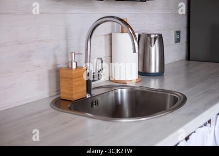l'intérieur de la cuisine présente un évier en acier inoxydable, un distributeur de savon en bois et une bouilloire, mettant l'accent sur un design minimaliste et une atmosphère lumineuse et aérée Banque D'Images