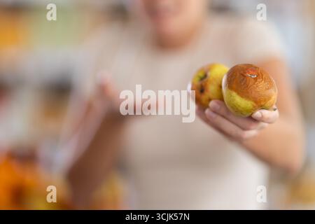 En magasin, la fille frustrée tient des fruits pourris dans les mains, gros plan Banque D'Images
