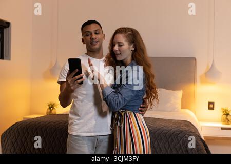 Jeune couple à la maison partageant un moment joyeux tout en regardant son smartphone Banque D'Images