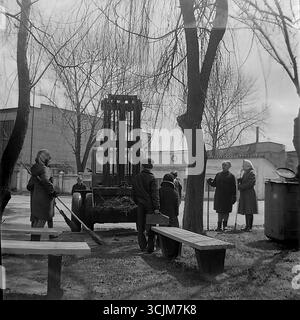 Un Subbotnik printanier dans une usine de Slavyansk en 1974 : des ouvriers, principalement des femmes, se reposent après avoir nettoyé le terrain, tandis qu'un chariot élévateur est chargé de branches et une cuisine de champ se trouve à proximité. Ce cliché, qui capture le rituel du travail collectif de l'époque de la stagnation, est un symbole de camaraderie, d'amélioration de la communauté et de la vie paisible et créative dans le Donbass Banque D'Images
