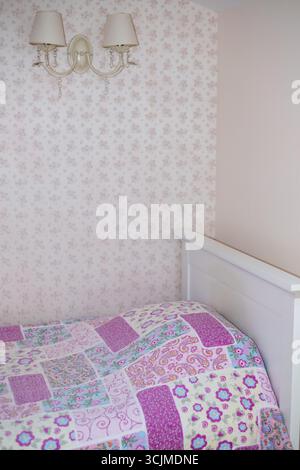 Couvre-lit coloré aux motifs complexes est élégamment placé sur un cadre de lit blanc dans une chambre à coucher légèrement éclairée, créant une atmosphère chaleureuse et accueillante Banque D'Images