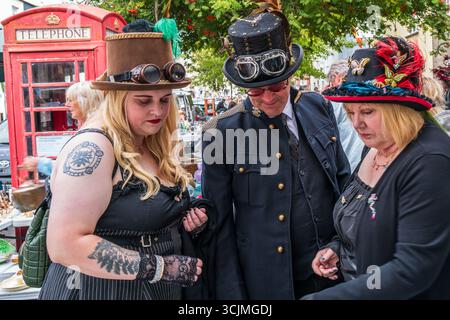 Trois individus en tenue steampunk, y compris des chapeaux et des costumes ornés, vus dans une rue publique pendant le Bridport Hat Festival 2025. Banque D'Images
