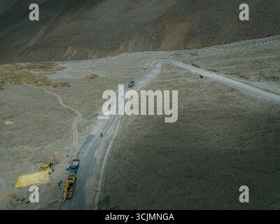 Vue aérienne d'une route sinueuse coupant à travers le paysage aride, où les véhicules naviguent sur le terrain près de matériel de construction, Kaza, Himachal Pradesh, Inde. Banque D'Images
