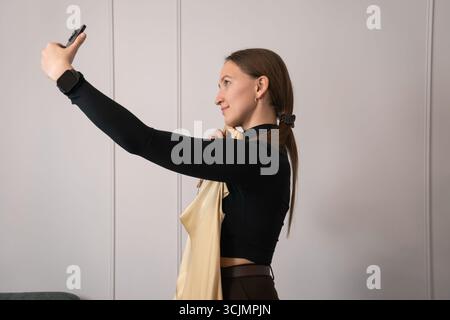 Créatrice de mode tenant une nouvelle robe sur un cintre et en prenant des photos avec son smartphone, créant du contenu pour les médias sociaux et la boutique en ligne Banque D'Images