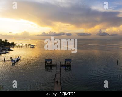 Vue aérienne d'une longue jetée en bois s'étendant dans les eaux tranquilles et ensoleillées sous un ciel enflammé aux teintes pastel, Key Largo, Floride, États-Unis. Banque D'Images
