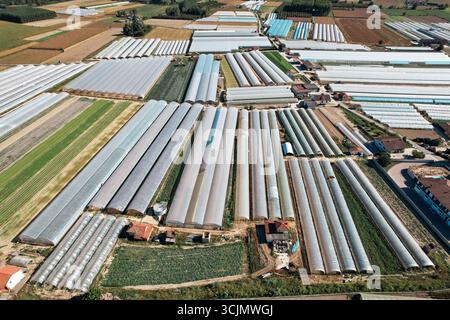 Vue aérienne d'un patchwork de serres reflétant le soleil, entrecoupé de blocs de champs labourés, créant une mosaïque agricole, Bra, Bra, Italie. Banque D'Images