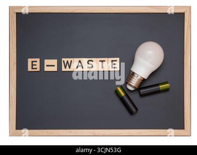 Tableau noir avec le mot « E-WASTE » fait de lettres en bois à côté d'une ampoule LED et de piles, symbolisant l'élimination responsable de devi électronique Banque D'Images