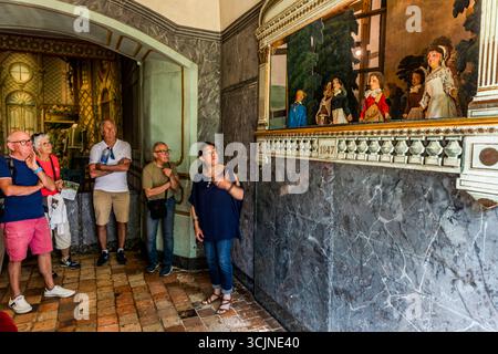 Un guide explique le théâtre de marionnettes à un groupe de visiteurs lors d'une visite guidée de la Maison de George Sand sur la Place Sainte-Anne à Nohant, commune de Nohant-Vic, dans le Berry, département de l'Indre, Centre-Val de Loire, France. La femme en haut bleu foncé et jeans se tient près d'un mur de marbre factice gris et pointe avec sa main gauche les marionnettes à gants derrière la balustrade portant l'année 1847. Cinq visiteurs écoutent, une femme tenant une brochure. L'arche sur la gauche offre une vue sur la toile peinte de la scène du théâtre. George Sand a écrit 80 pièces. Elle avait la Banque D'Images
