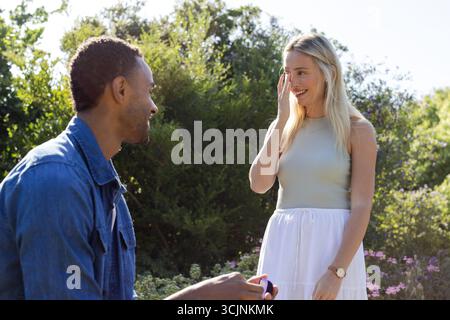 Homme proposant à la femme surprise dans le jardin, créant un moment joyeux et romantique Banque D'Images