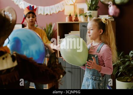 Fille caucasienne tenant un ballon avec divers enfants célébrant l'anniversaire Banque D'Images