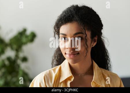 Portrait d'une jeune femme afro-américaine aux cheveux bouclés regardant la caméra à la maison. Banque D'Images