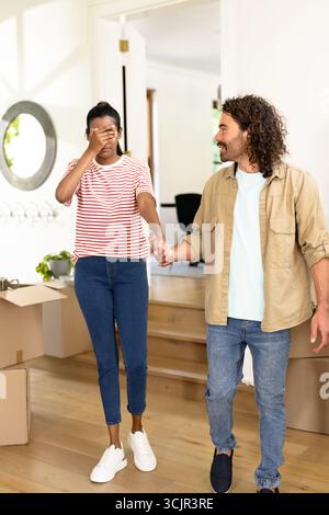 Jeune couple diversifié tenant la main, explorant une nouvelle maison avec excitation et curiosité Banque D'Images