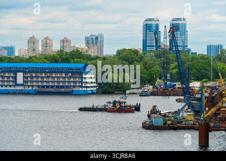 Plan large d'une rivière animée avec diverses péniches, grues de construction, et une ligne d'horizon de la ville par une journée nuageuse et nuageuse Banque D'Images