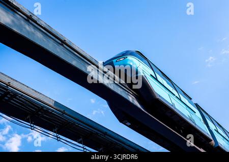 Train monorail moderne circulant sur des voies surélevées contre un ciel bleu clair. Banque D'Images