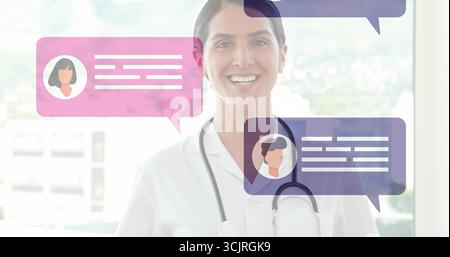 Médecin féminin souriant debout dans la clinique portant manteau blanc et stéthoscope avec des bulles de chat Banque D'Images