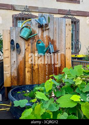 Fonction d'eau de jardin créative fabriquée à partir d'arrosoirs vintage montés sur un panneau de bois, faisant couler l'eau dans un bassin. Banque D'Images