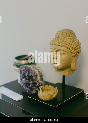 Une statue de Bouddha se dresse parmi des cristaux et une fleur de lotus, créant une atmosphère paisible dans un cadre intérieur moderne. Banque D'Images