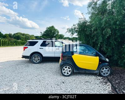 Kiev, Ukraine - 10 août 2025 : voiture compacte Smart fortwo jaune garée à côté d'un plus grand VUS blanc Ford Explorer sous un ciel lumineux Banque D'Images