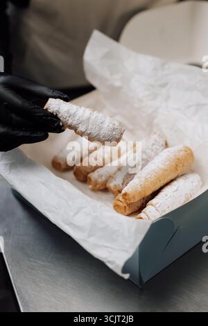 Cornes de crème fraîchement cuites dans du sucre en poudre tenues dans la main sur la boîte à pâtisserie Banque D'Images