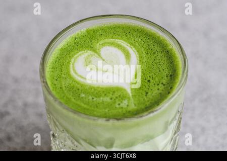 Un verre de latte matcha crémeux avec un motif latte en forme de cœur sur le dessus. La boisson verte vibrante est servie dans un verre clair texturé Banque D'Images