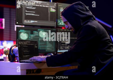 Pirate exécute un script de codage sur ordinateur portable pour violer la sécurité de l'entreprise et ouvrir des bases de données verrouillées. Homme à capuche utilisant un ordinateur portable, faisant des cyberattaques, exploitant des plates-formes de piratage sur ordinateur Banque D'Images