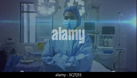 Chirurgienne debout croisant les bras sous les lumières chirurgicales dans la salle d'opération, avec plateaux de moniteurs Banque D'Images