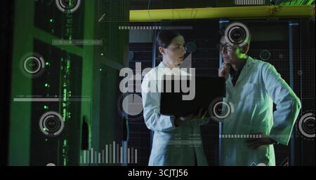 Analysant les données des techniciens de laboratoire tenant l'ordinateur portable dans la salle des serveurs avec des racks, des câbles, des superpositions de données Banque D'Images