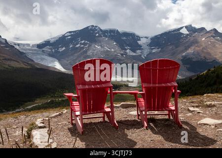 Deux chaises rouges emblématiques de Parks Canada offrent un avant-plan frappant à une vue spectaculaire du champ de glace Columbia depuis le sentier Wilcox Pass en Alberta. Banque D'Images