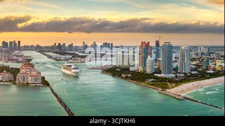 Luxueux paquebot de croisière naviguant au port de Miami via le chenal principal près de South Beach. Hôtels et bâtiments résidentiels sur le front de mer et hi Banque D'Images