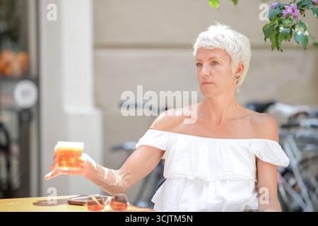 Une femme en chemise blanche tient un verre de thé. Elle est assise à une table avec un vélo derrière elle Banque D'Images