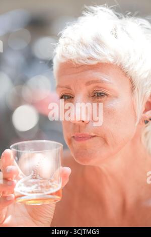 Une femme tient un verre d'alcool. Elle regarde le verre et semble profiter de sa boisson Banque D'Images