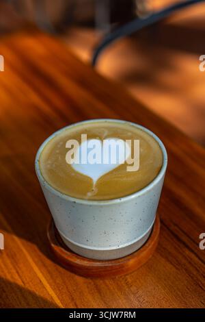 Gros plan d'un latte avec des œuvres d'art en forme de cœur dans une tasse posée sur une table en bois. Parfait pour le café et les thèmes des boissons. Banque D'Images