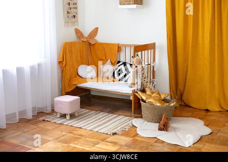 Design intérieur moderne d'une chambre d'enfant. Jardin d'enfants. Chambre de bébé scandinave : berceau en bois avec literie, oreillers, panier avec jouets, pouf et tapis Banque D'Images