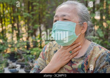 Femme senior portrait en plein air portant un masque facial médical jetable et mal de gorge de toux. Concept de santé senior. Banque D'Images