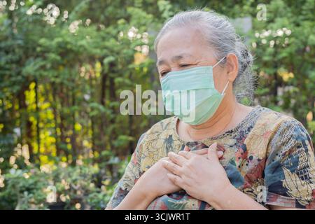 Portrait de vue de côté d'une femme âgée portant un masque facial protecteur à l'extérieur et douleur thoracique de toux. Copier l'espace. Banque D'Images