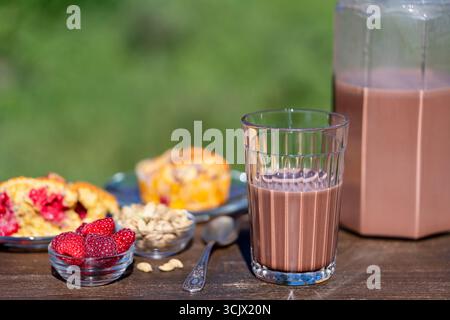 Indien masala chai ou thé ou cacao en verre avec cruche et muffin à la framboise sur la table en bois dans le café sur fond de nature, de près. Trendy Healthy d Banque D'Images