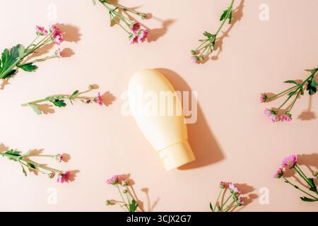 Bouteille cosmétique jaune et petites fleurs roses sur fond neutre avec lumière et ombres. Vue de dessus, pose à plat, maquette. Banque D'Images