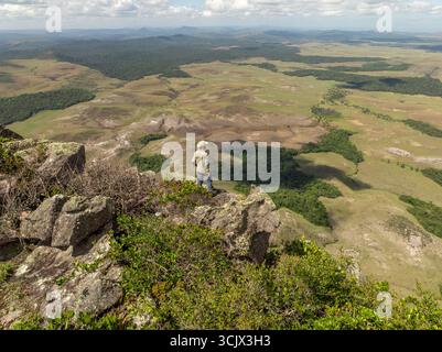 Vue aérienne d'une figure solitaire debout au sommet d'un terrain rocheux, regardant au-dessus de la vaste étendue verte de Chiricayen Tepui, Santa Elena de Uairen, Venezuela. Banque D'Images