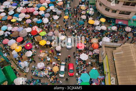 Accra, Ghana - 23 mars 2024 : vue aérienne du chaos animé du marché de Makola, où des parapluies colorés fleurissent au-dessus des foules animées et des véhicules naviguent dans les rues étroites. Banque D'Images