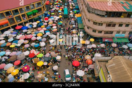 Accra, Ghana - 23 mars 2024 : vue aérienne du chaos vibrant du marché de Makola, où convergent une mosaïque de parapluies colorés et une foule animée, créant une tapisserie animée de commerce et de communauté. Banque D'Images