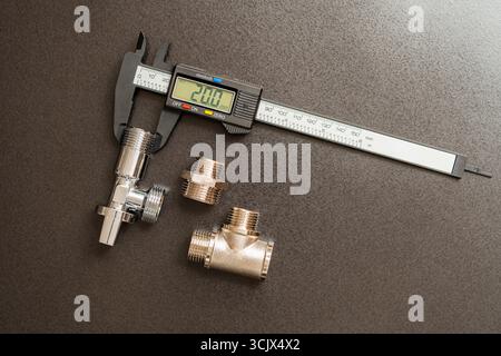 Mesure du diamètre des adaptateurs de plomberie avec un pied à coulisse électronique numérique, gros plan, vue de dessus. Concept de réparation de plomberie Banque D'Images
