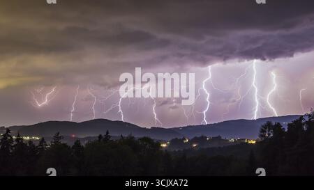 Vue des éclairs dentelés frappant vers le bas des nuages de tempête couvant, éclairant les collines silhouettées et les lumières de la ville lointaine ci-dessous, Graz, Styrie, Banque D'Images