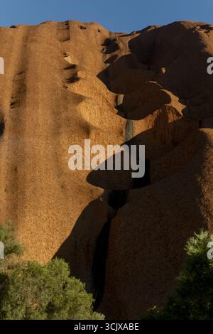 Vue sur le massif monolithe de grès baigné de soleil, sa surface texturée sculptée par le temps, s'élève majestueusement contre le ciel bleu profond, Uluru, Nort Banque D'Images