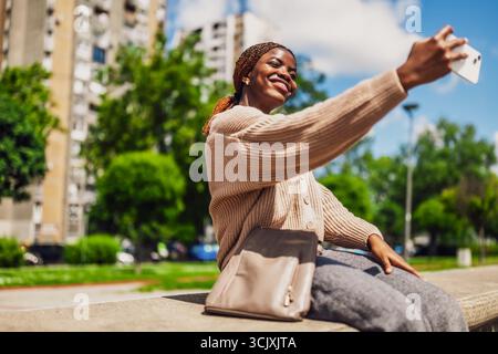 Jeune femme Noire heureuse prend selfie un jour ensoleillé avec son smartphone. Banque D'Images