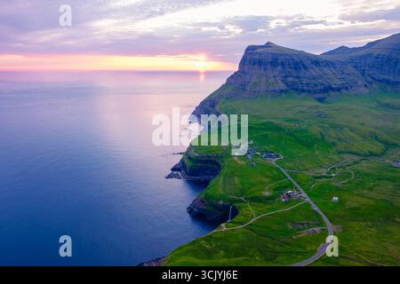 Les falaises à couper le souffle s'élèvent de façon spectaculaire des eaux calmes au coucher du soleil dans les îles Féroé. Des paysages verdoyants entourent de petites colonies, la cascade de Mulafossur près du village de Gasadalur Banque D'Images