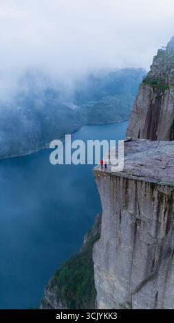 Deux courageux aventuriers se tiennent au bord de la falaise Preikestolen, surplombant les eaux sereines du Lysefjorden. Banque D'Images
