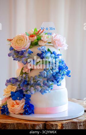 Élégant gâteau de mariage à trois niveaux orné d'un spectacle en cascade de pivoines artificielles et d'hortensias Banque D'Images