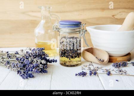 Huile de lavande infusée à froid maison. Huile d'olive recouvrant les fleurs de lavande séchées dans un bocal en verre. Un mortier et un pilon, avec un paquet de fleurs de lavande. Banque D'Images
