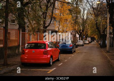 Rouge Volkswagen polo et d'autres voitures garées dans une rue calme de Belgrade avec des arbres d'automne et des immeubles d'appartements. District de Zvezdara. Belgrade, Serbie - Banque D'Images